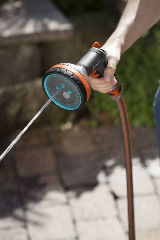 Een hand houdt een grijze Gardena sproeikop met oranje en blauwe accenten vast, er komt een waterstraal uit.