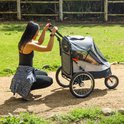 Vrouw in sportkleding knielt naast een grijze hondenbuggy met een hond erin. De buggy heeft gaas voor ventilatie.