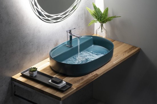 Ovaal petrolgroene wastafel op een houten blad, met kraan en stromend water.