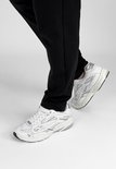 Voeten in witte "DUTCH'D" sneakers met zilveren details, staand op de grond.
