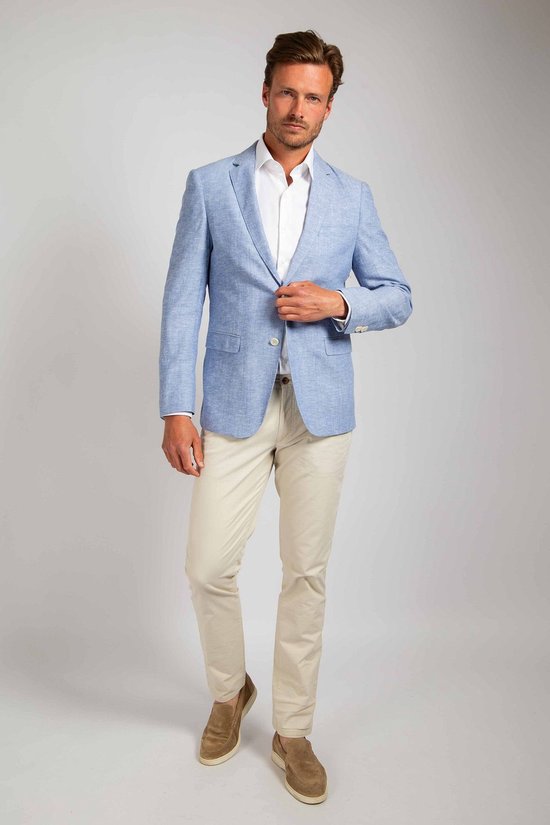 Man met lichtblauwe linnen blazer, wit overhemd en beige broek. Blazer is open en hij houdt de revers vast.
