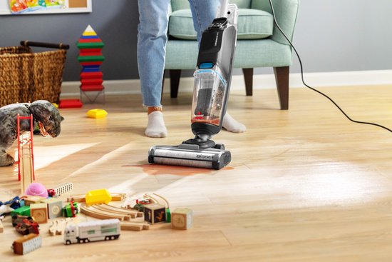Een vrouw met spijkerbroek en witte sokken gebruikt de BISSELL CrossWave vloerreiniger om een houten vloer met rode vlekken schoon te maken.