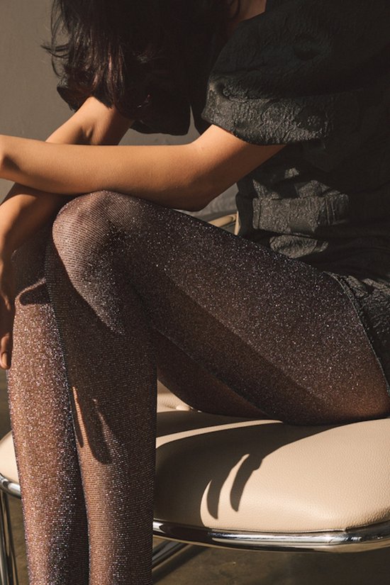 Vrouw zittend met zwarte jurk en glinsterende panty