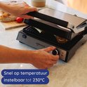 Handen draaien aan de knop van een Safecourt contactgrill. De tekst geeft aan: "Snel op temperatuur, instelbaar tot 230°C".