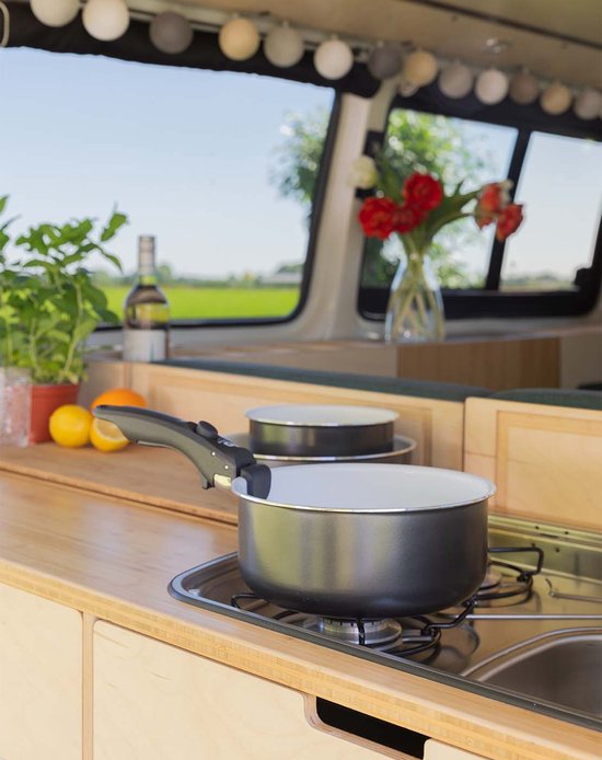 Donkergrijze kookpan met witte binnenkant, op een gasfornuis in een camper.