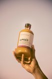 Een hand houdt een fles GIMBER Original omhoog tegen een pastelkleurige achtergrond.