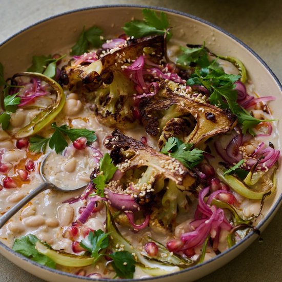 Gegrilde bloemkool met witte bonen, granaatappelpitjes, rode ui en sesamzaadjes in een romige saus.