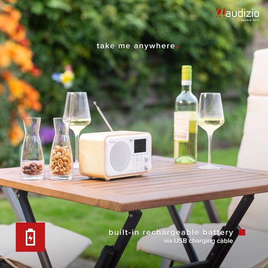 DAB radio met wit front en houten kast op een tuintafel, naast glazen en flessen.