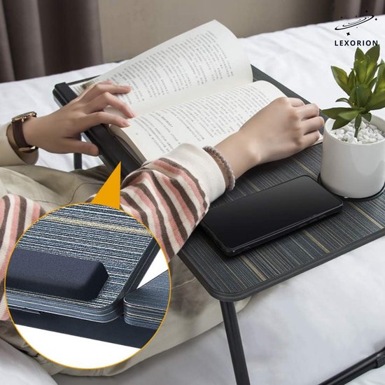Dichtbij van een laptoptafel met een gestreept oppervlak, een boek, een plant en een telefoon.