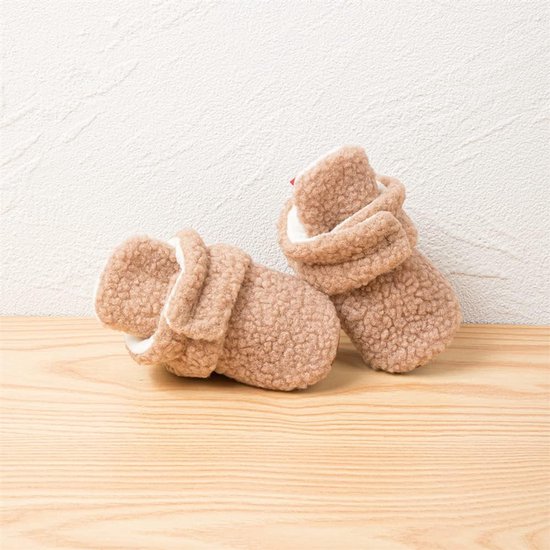 Paar bruine teddy babyslofjes met opgerolde boord, witte voering, op houten plank.