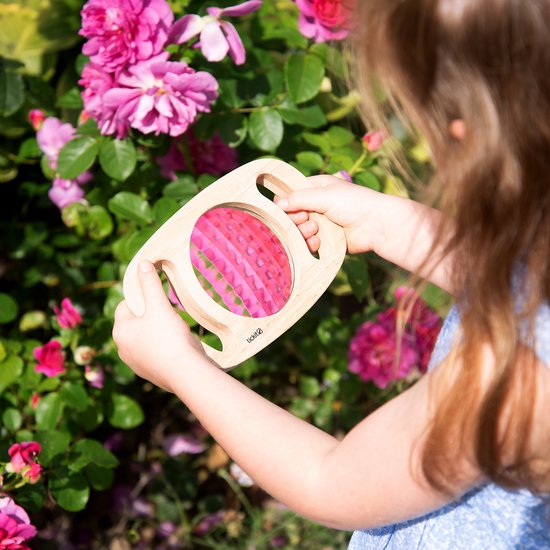 Enfant tenant un kaléidoscope en bois avec des motifs roses près de roses.