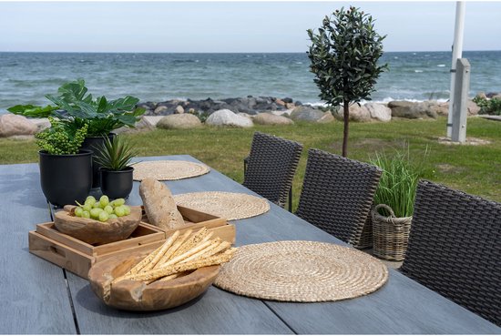 Houten eettafel met ronde rieten placemats, broodstengels en druiven.