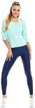 Vrouw in een mintgroene loszittende top met driekwart mouwen en een donkerblauwe glanzende legging, witte sneakers.