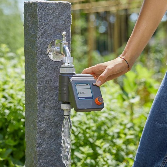 Hand bedient GARDENA besproeiingscomputer aan kraan. Water stroomt uit de slang.