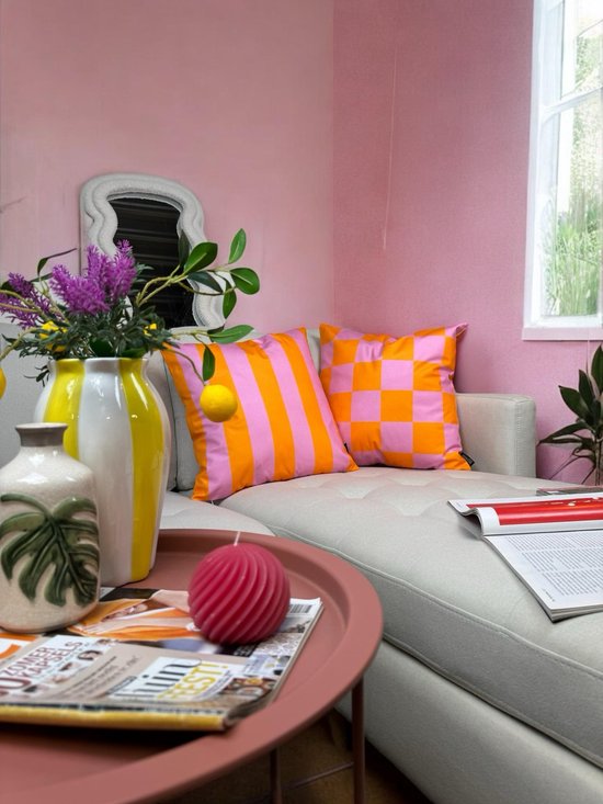 Twee kussens, een met oranje en roze strepen, de ander met oranje en roze ruiten, op een lichte bank.