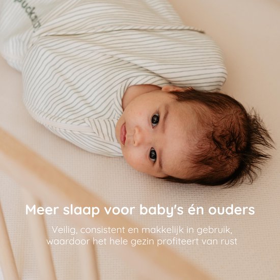 Baby ingewikkeld in een groen gestreept Puckababy slaapzakje in een ledikant.