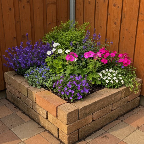 Verhoogde border met diverse bloeiende planten: paars, roze, wit en blauw, tegen een houten schutting.