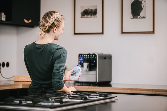 Een vrouw met een vlecht giet ontkalker uit een fles in een espressomachine.