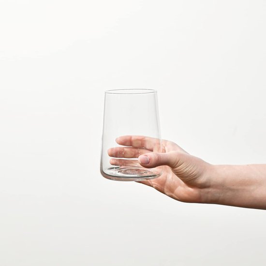Een hand die een hoog, transparant glas vasthoudt tegen een witte achtergrond.