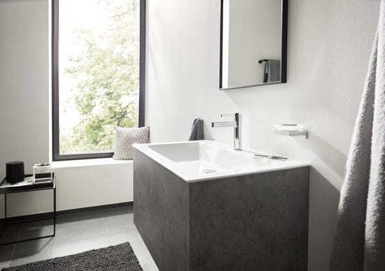 Een badkamer met een grijze wastafelonderkast, een chromen kraan en een grote raampartij.