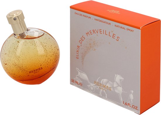 Elixir des Merveilles eau de parfum in een ronde, oranje flacon met gouden dop, bezaaid met gouden glitters. Naast de flacon een doos met paard en koets.