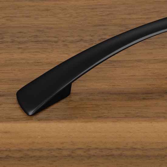 Close-up van een gebogen, zwarte meubelgreep op een houten oppervlak.