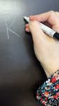 Hand met witte stift tekent de letter 'K' op een zwart magnetisch krijtbord.