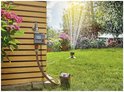 Gardena besproeiingscomputer, aangesloten op een kraan, met sproeiende sprinkler in de tuin.