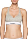 Model in grijze Calvin Klein bralette met V-hals, racerback en wit logo-elastiek.