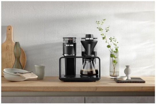 Zwart filterkoffiezetapparaat met glazen kan, koffiebonenreservoir en bedieningspaneel.