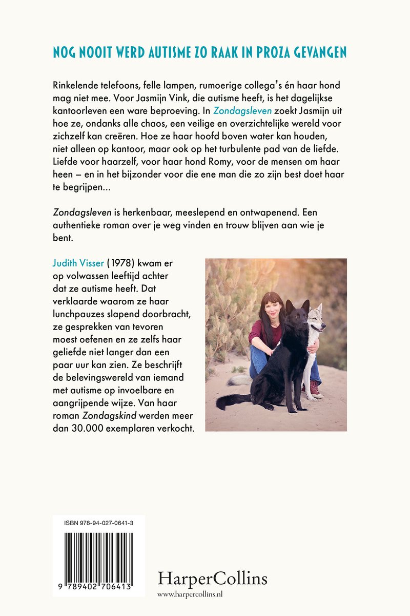 Judith Visser zit met twee honden, een zwarte en een witte, op de grond. Ze draagt een blauw vest en een grijze broek.