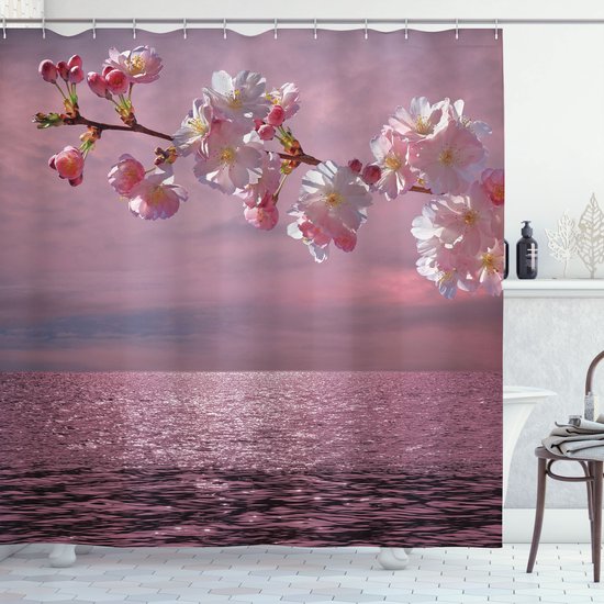 Une branche de cerisier en fleurs au-dessus de l'eau scintillante d'un océan au coucher du soleil.