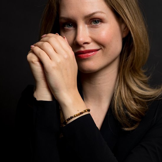 Model draagt een armband met tijgeroogkralen en gele goudkleurige kralen aan haar linkerpols.