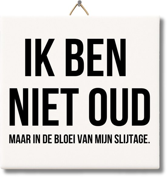 Wit keramisch tegeltje met de zwarte tekst 'IK BEN NIET OUD MAAR IN DE BLOEI VAN MIJN SLIJTAGE.' en een ophanghaakje.