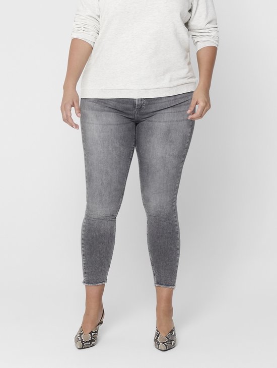 Model in een lichtgrijs shirt en grijze skinny jeans met rafelige zoom, met beige pumps.
