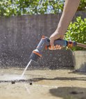 Hand met GARDENA Comfort EcoPulse spuitpistool, sproeit water op een betonnen ondergrond.