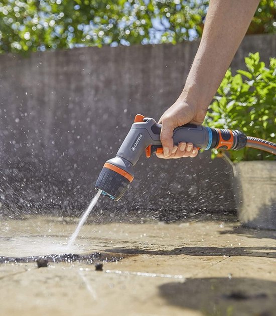 Hand met GARDENA Comfort EcoPulse spuitpistool, sproeit water op een betonnen ondergrond.