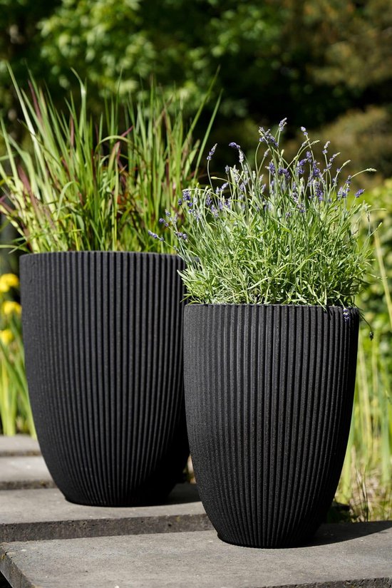 Twee zwarte, geribbelde bolvormige bloempotten met gras- en lavendelplanten.