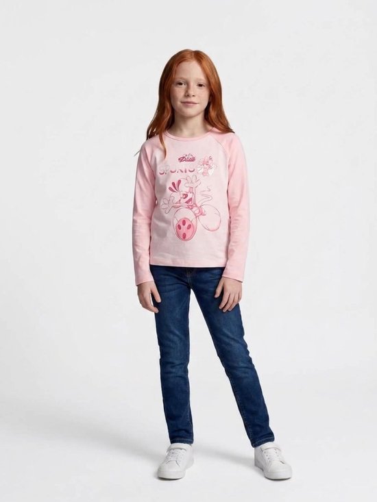 Model draagt een roze Diddl Sports-longsleeve met spijkerbroek en witte sneakers.