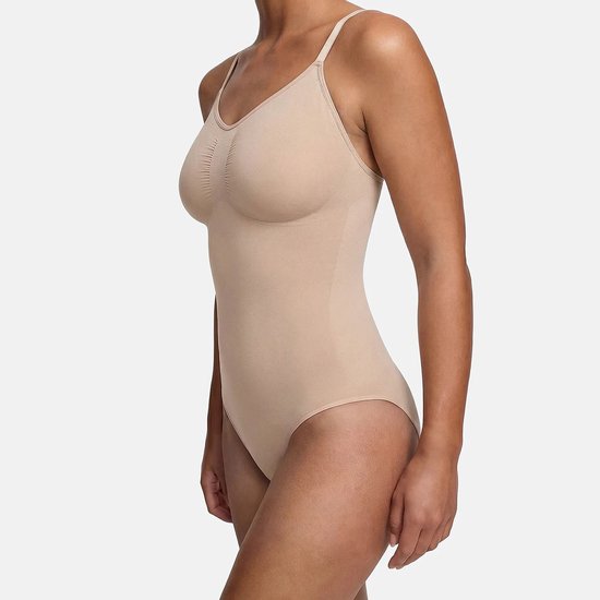 Zijaanzicht van een beige corrigerende bodysuit met dunne bandjes en gerimpeld detail op de borst op een model.