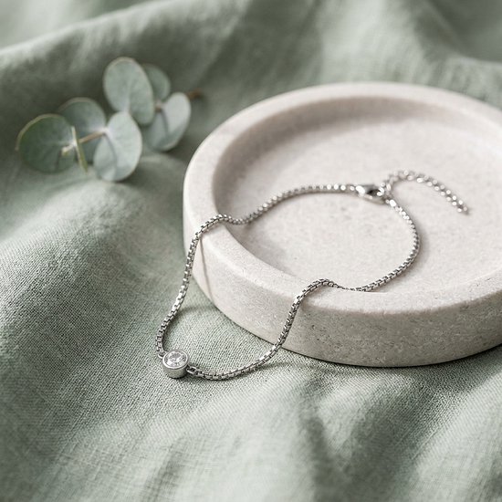 Zilveren armband met zirkonia rustend op een stenen schaaltje op een groen linnen doek met eucalyptusblad.