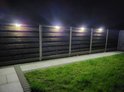 Meerdere solarlampen bevestigd aan een houten schutting, die een tuinpad verlichten in het donker.