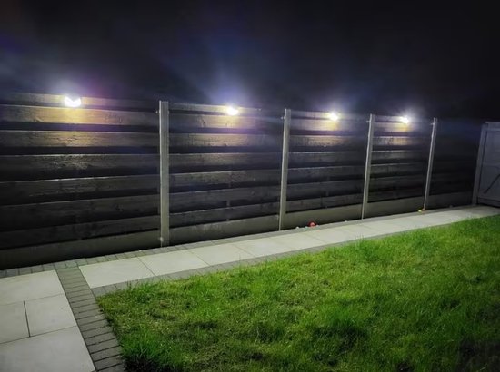 Meerdere solarlampen bevestigd aan een houten schutting, die een tuinpad verlichten in het donker.