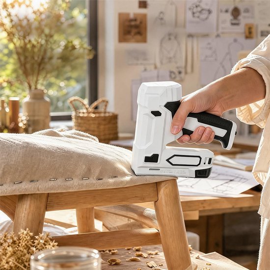 Handen gebruiken een wit-zwart nietpistool om beige stof vast te zetten op een houten meubel.