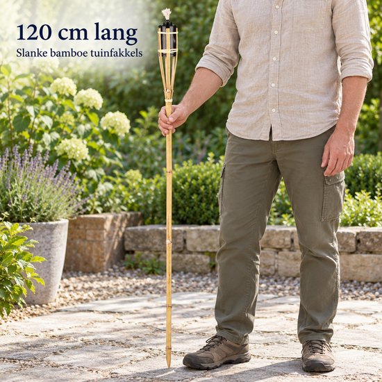 Man in een lichte blouse en olijfgroene broek houdt een 120 cm lange bamboe tuinfakkel vast.