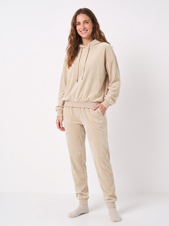 Model draagt een beige fleece huispak met hoodie en bijpassende joggingbroek met boorden.