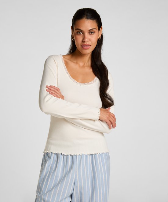 Model met armen over elkaar in een crème-wit ribgebreid shirt met kanten accenten en een lichtblauwe gestreepte broek.