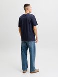 Achterkant van een man in een marineblauw T-shirt en wijde jeans met beige instappers.