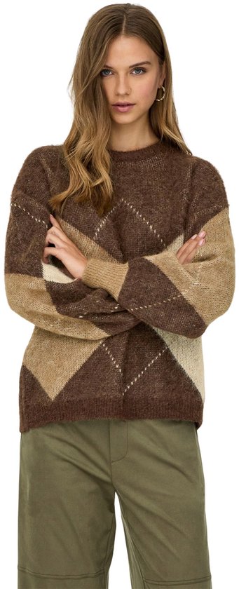 Model met gekruiste armen draagt een bruine, beige en crème gemêleerde gebreide trui met ruitpatroon en groene broek.