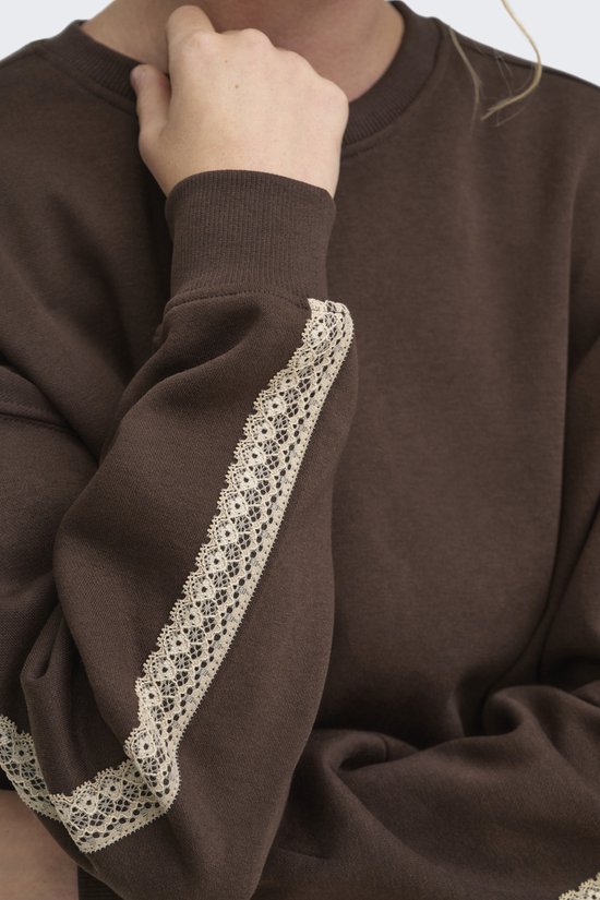 Detailopname van een bruine trui met beige kanten bies langs de mouw.
